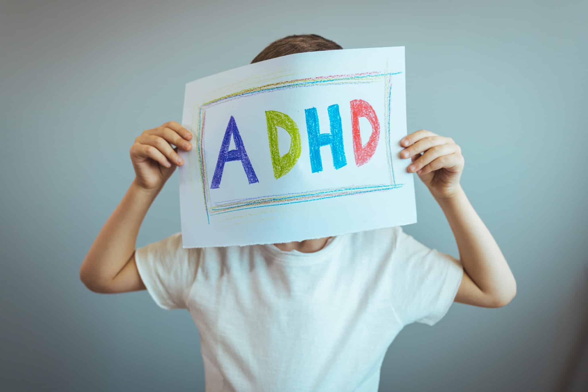 boy holds ADHD text written on sheet of paper.