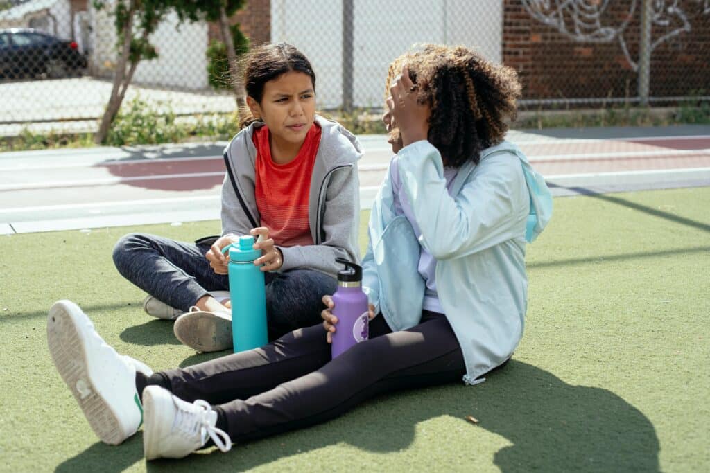 Two girls sitting outdoors with water bottles, enjoying a break from activity.