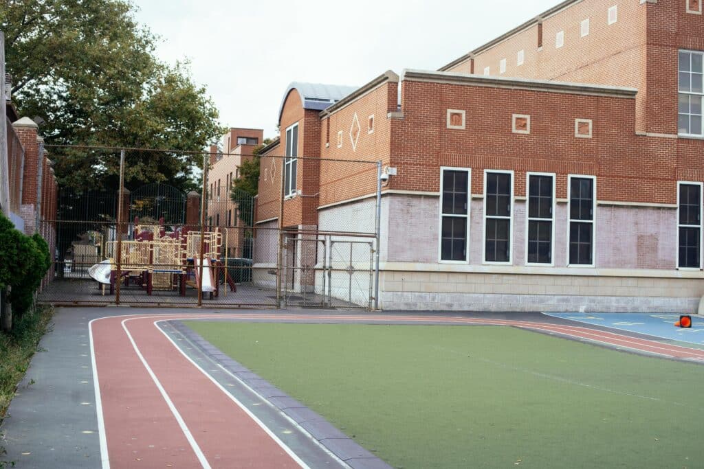Empty urban schoolyard featuring a red brick building, playground, and athletic track, captured during daytime.