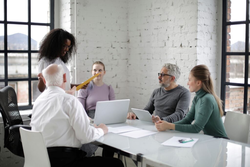 Group of multiethnic coworkers sitting at table with netbooks and papers while black woman explaining project
